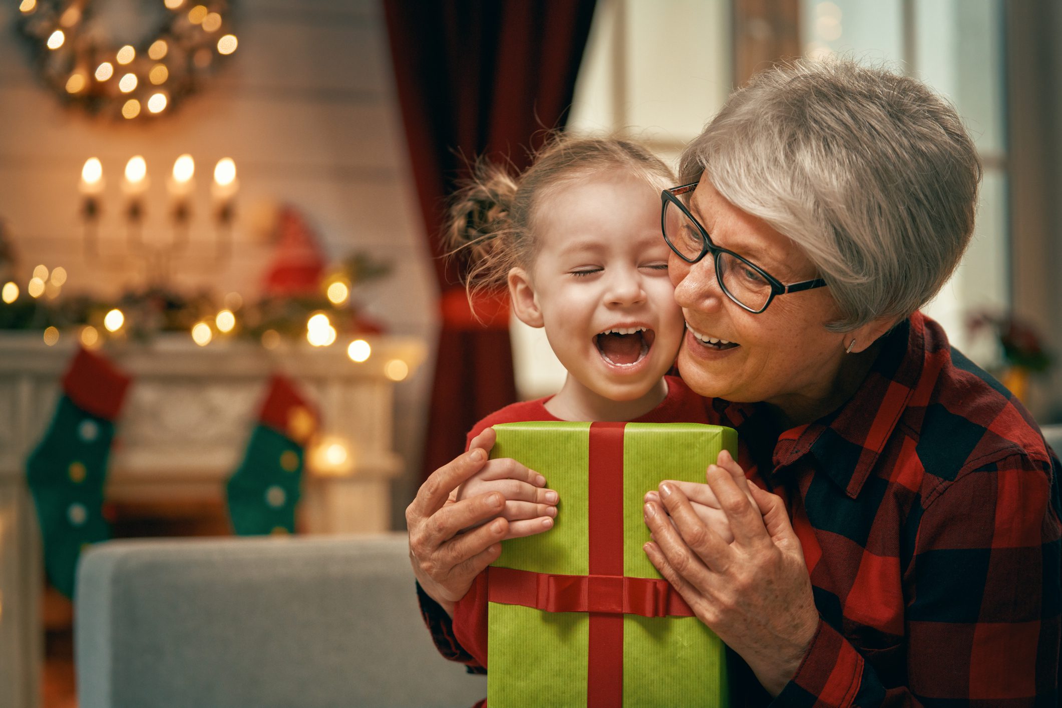 family near Christmas tree A grandmother hugs her granddaughter who is holding a holiday present.