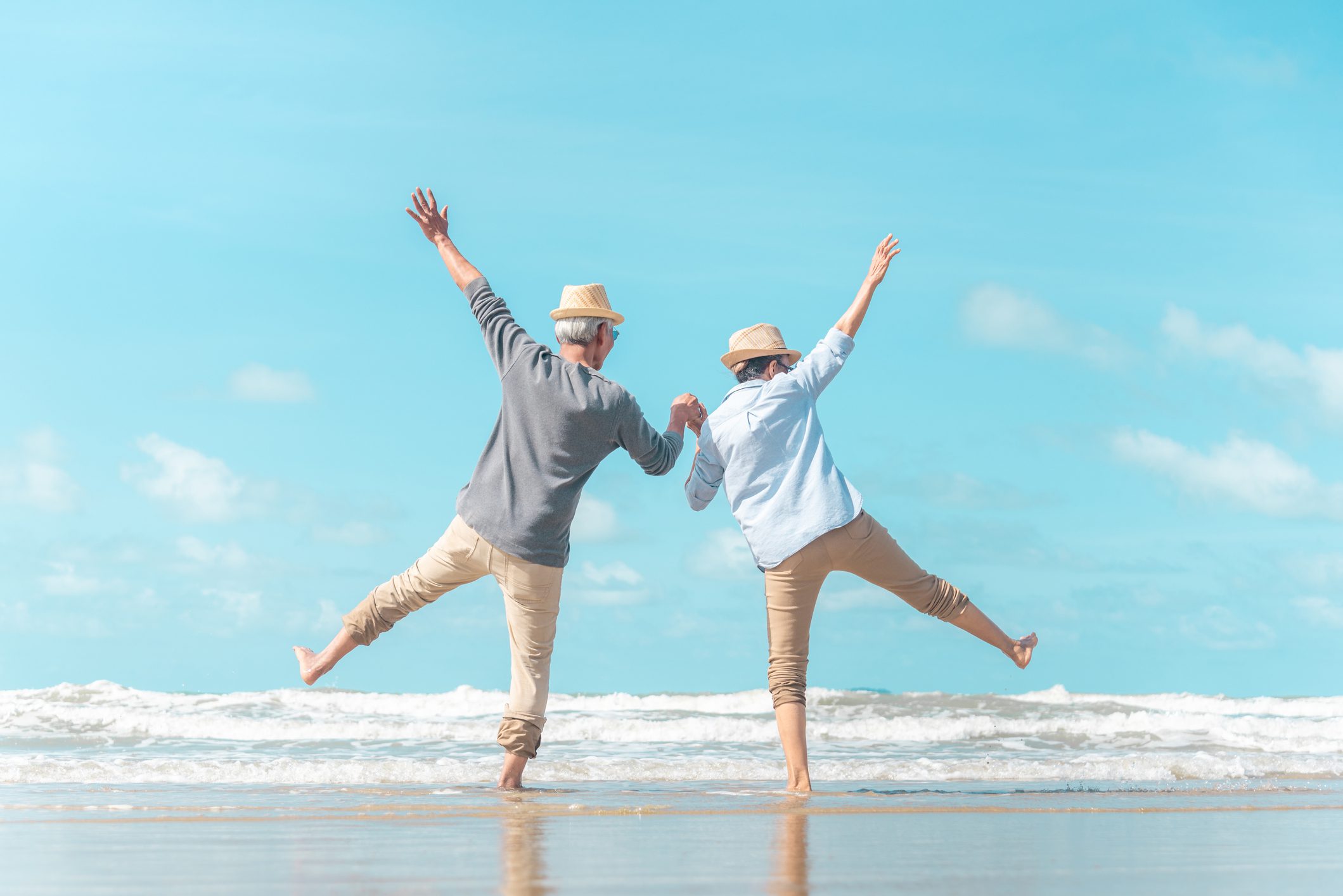A 55+ couple enjoys a fun walk on the beach, kicking up their feet in shallow water.